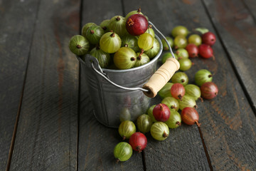 Red and green gooseberry in pail on wooden table close-up