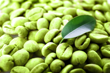 Heap of green coffee beans with leaf close up