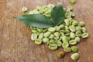 Heap of green coffee beans with leaves on table close up