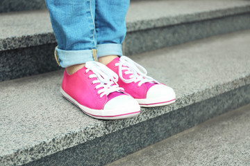 Fototapeta na wymiar Female feet in pink gumshoes on stone stairs