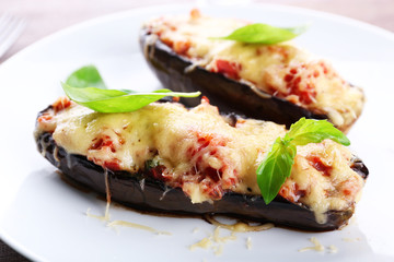 Dish of eggplant with cherry tomatoes and cheese in white plate on wooden table, closeup
