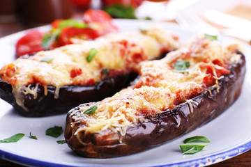 Dish of eggplant with cherry tomatoes and cheese in white plate on wooden table, closeup
