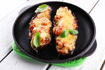 Dish of eggplant with cherry tomatoes and cheese in black pan on wooden table, closeup
