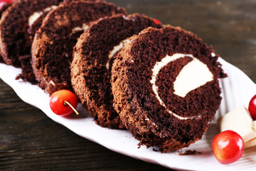 Delicious chocolate roll in white plate on wooden table, closeup