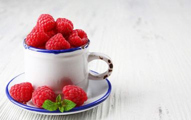 Fresh red raspberries in cup on wooden background