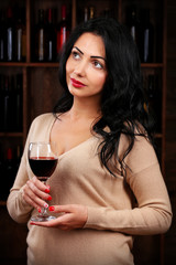 Pretty young woman with wineglass on wine shelf background