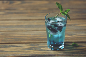 Glass of cold refreshing summer drink with berries and ice cubes on table close up