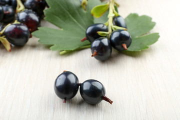 Pile of black currants with green leaves on wooden background