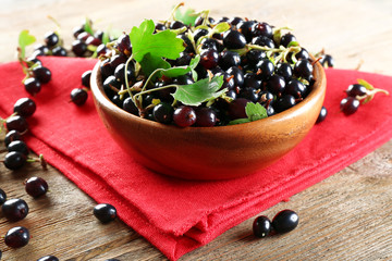 Obraz na płótnie Canvas Ripe black currants in bowl on wooden table with red napkin, closeup