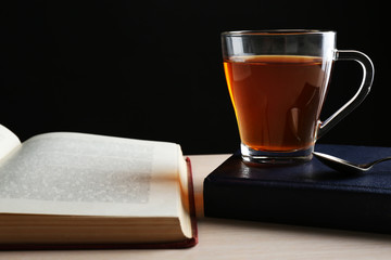 Glass cup of tea with books on wooden table on black background