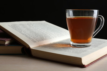 Naklejka premium Glass cup of tea with book on wooden table on black background