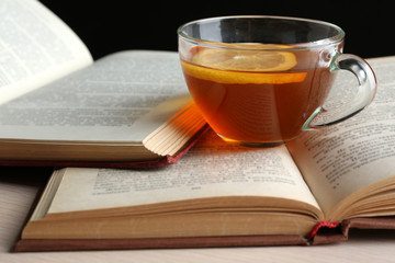 Glass cup of tea with open books on wooden table, closeup