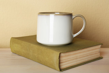 Cup of tea with book on wooden table on light wall background