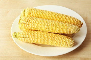 Fresh corn on cobs in plate on wooden table, closeup