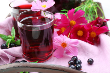 Obraz na płótnie Canvas Glasses of fresh blackcurrant juice on wooden tray with pink napkin and flowers, closeup