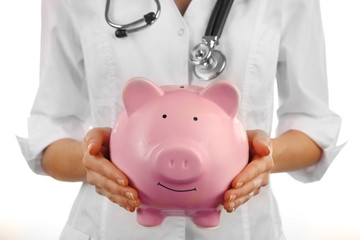 Doctor in white uniform with stethoscope holding pink piggy bank isolated on white