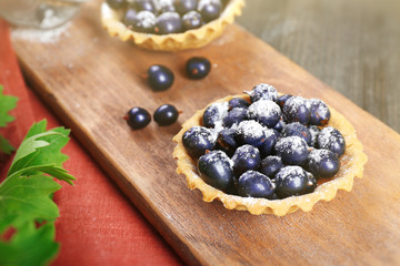 Delicious crispy tarts with black currants on wooden cutting board, closeup