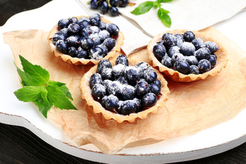Delicious crispy tarts with black currants on parchment on wooden board, closeup