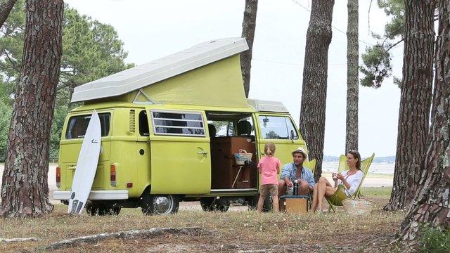 Happy family relaxing by camper van in summer