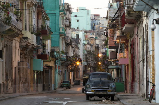 Street scene before sunrise showing dilapidated buildings crowded together and vintage American cars, Havana Centro, Havana, Cuba