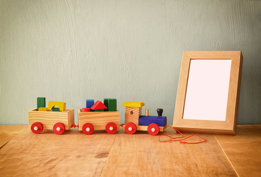 Wooden toy train over wooden table next to photo blank frame