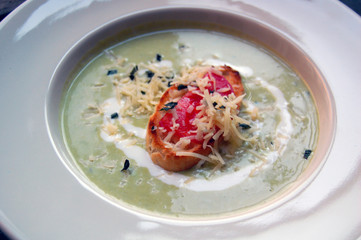 close up of green pea soup with bread and cheese on top