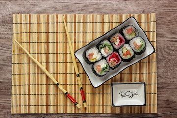 Sushi rolls on a plate on bamboo brown straw mat  with chopsticks top view