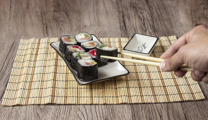 Hand holding sushi roll using chopsticks on wooden background.Sushi set.