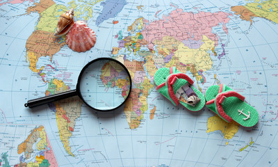 Plan travel. Map of the world, magnifying glass, shell, flip-flops on the map background.