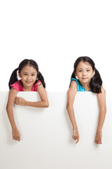 Fototapeta na wymiar Happy Asian twins girls behind white blank banner