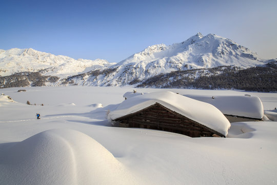 Some Spluga huts near the Maloja Pass submerged by meters of powder snow on a clear winter day, Graubunden, Swiss Alps