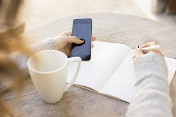 girl writes in a notebook, with cell phone and cup of coffee