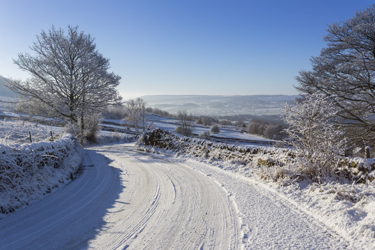 Snowy, bendy country lane with stone walls and trees, Curbar Edge, Peak District National Park, Derbyshire