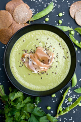 Healthy green soup with ham and peas on a black background