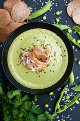Healthy green soup with ham and peas on a black background