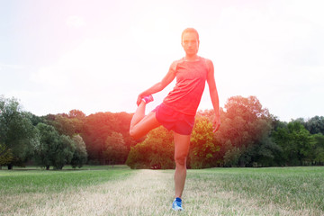 Athletic woman warming up before her morning workout in park grass. Runner training outdoors, healthy lifestyle concept.