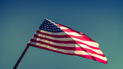 American flag with stars and stripes hold with hands against blu