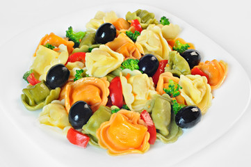 Salad made with tortellini, olives, broccoli, red pepper, on a plate, white background
