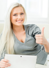 Young and happy blond woman with a tablet holding thumbs up