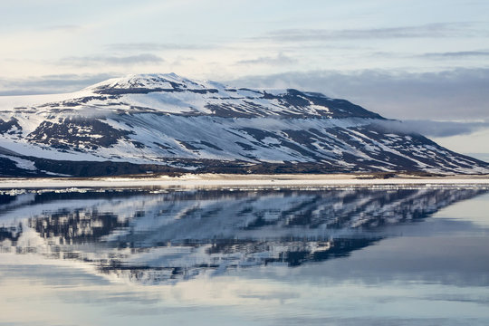 Snow-capped mountains reflected in the calm waters of Olga Strait, Svalbard, Arctic