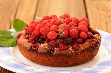 Homemade round chocolate cake with fresh raspberries and green l
