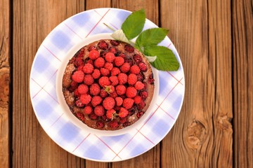 Homemade round chocolate cake with fresh wild raspberries and gr