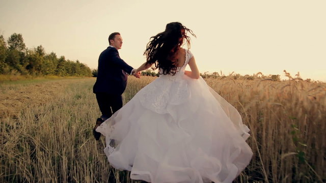 Bride and groom running on the field with wheat HD
