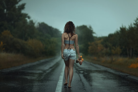 Girl back. Walks on the road. Under rain.