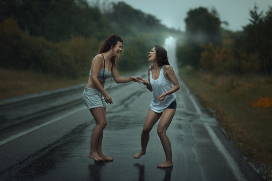 Girls standing in the rain on roadway.