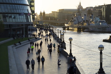 Pedestrians silhouetted on More Place riverfront with City Hall and HMS Belfast behind, London