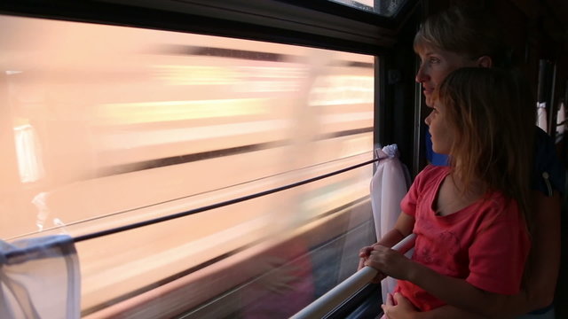 Woman with daughter ride in a train, they look out the window
