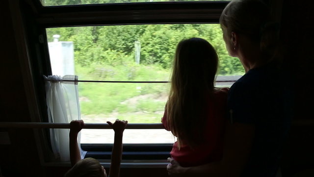 Woman with daughter and son ride in a train, they look out the window

