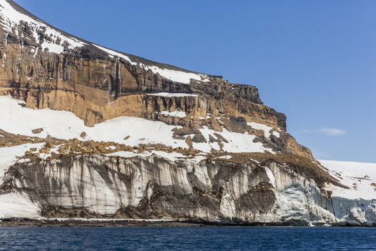 Rust-colored volcanic tuff cliffs above a dark material filled glacier at Brown Bluff, eastern side of the Tabarin Peninsula, Weddell Sea, Antarctica