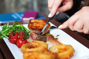 Mädchen isst Filetsteak mit fritierten Zwiebelringen, gebackenen Kartoffelstreifen und Salat